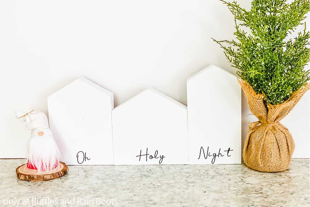 Three white house shapes on holiday background with oh holy night in vinyl along the bottom cut with a Cricut.