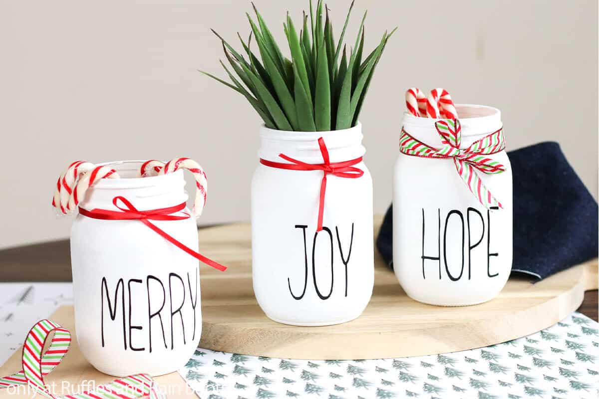 A set of white farmhouse painted jars made for Christmas using the Cricut machine, red ribbon, and filler.