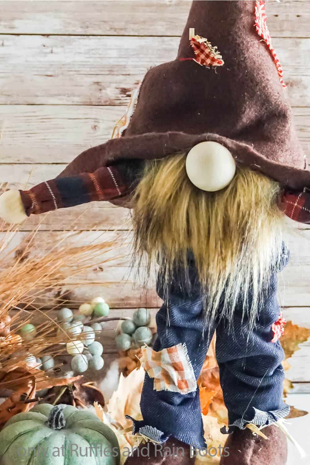 A close up of a cute fall scarecrow gnome that stands wearing jeans, boots, and a patch hat.
