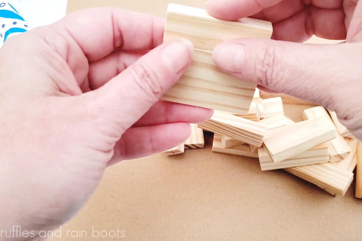 horizontal image of hands using wood glue to secure the dollar tree tumbling blocks together in a stack of three for the magnet base