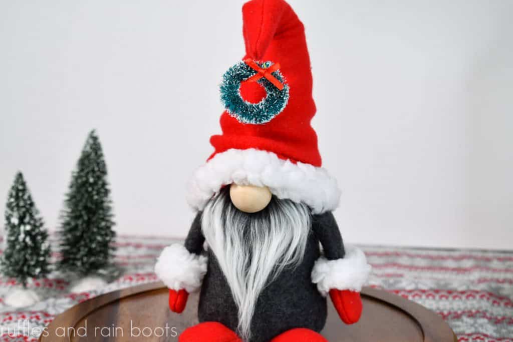 horizontal image of a Christmas gnome with a holiday wreath accent in a red gnome hat gray body and adorable mittens and shoes