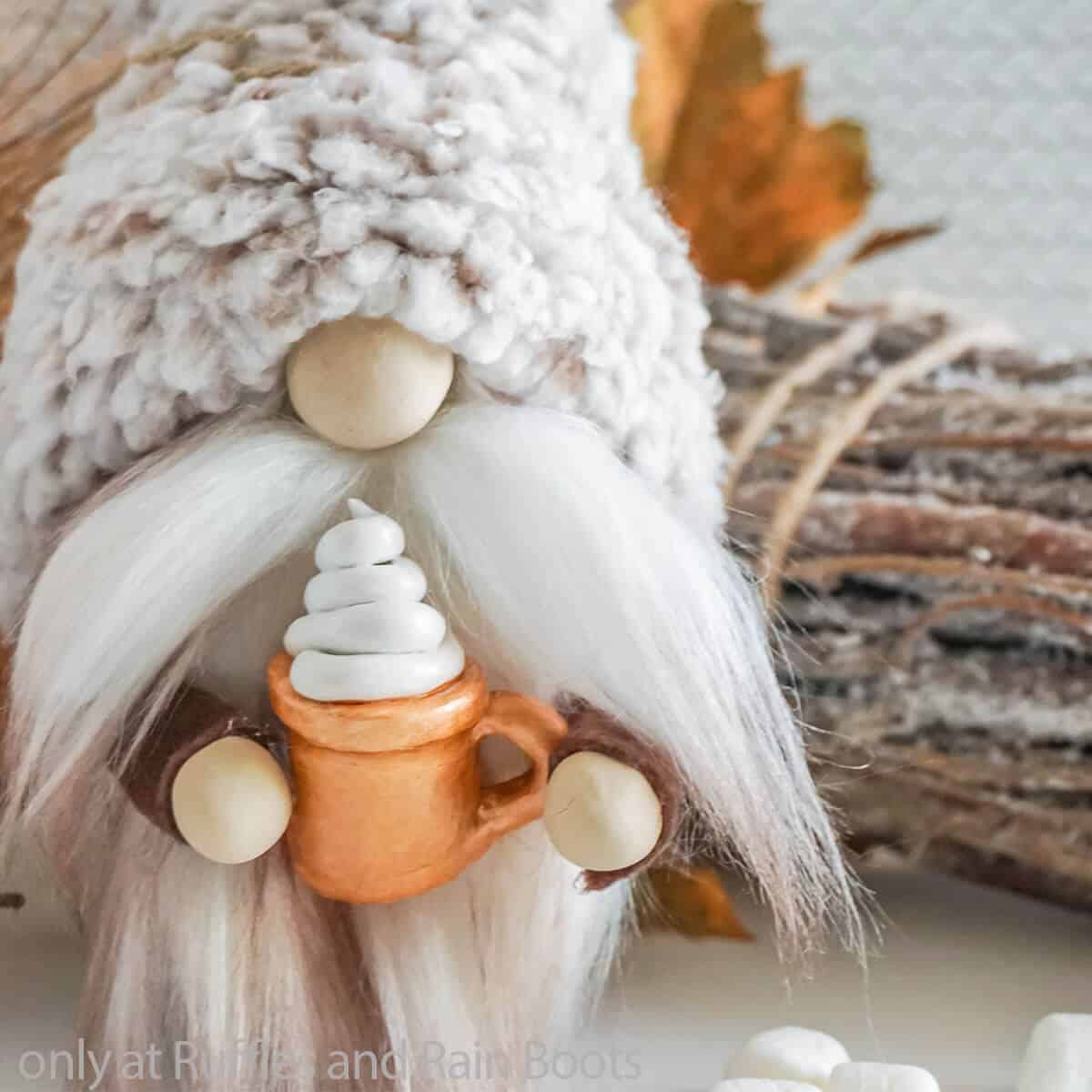 Close up image of an adorable gnome with a fuzzy hat holding a copper hot cocoa mug with whipped cream. 