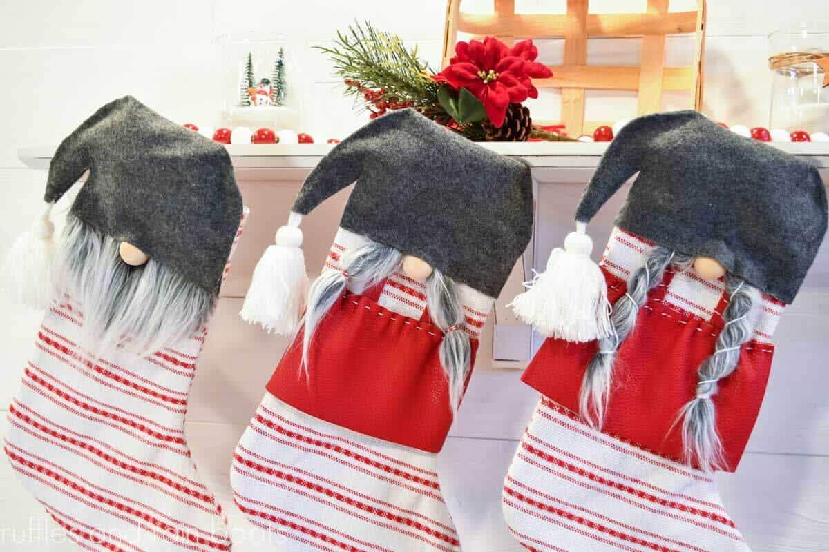 horizontal image of three no sew gnome stockings in red white and gray hanging on white shelf on white shiplap wall with holiday decorations styled for Christmas