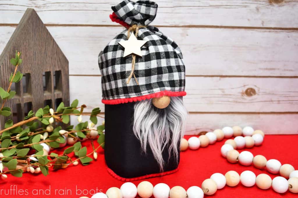 horizontal image of Christmas gnome jar wrap made with a placemat on a holiday background with farmhouse beads and wood house
