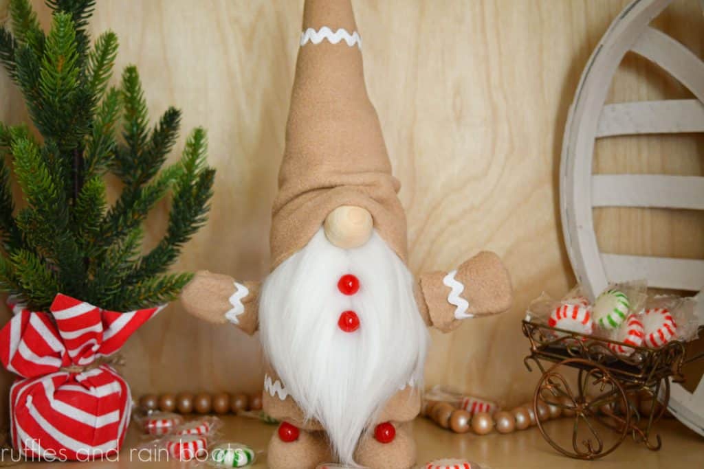 horizontal image of gingerbread gnome made with hot glue and fleece on a Christmas background with mini tree and candy