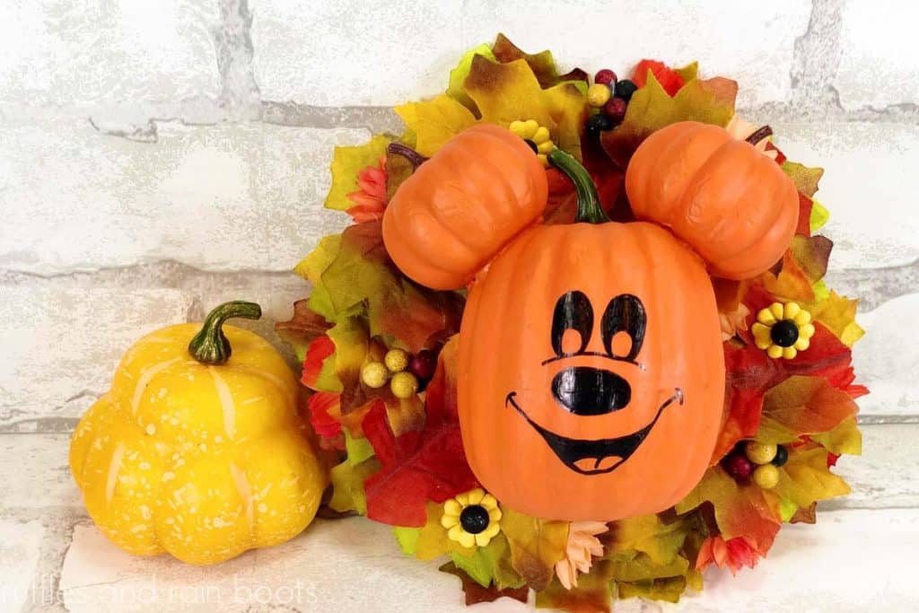 horizontal image close up of fall Mickey Mouse wreath of pumpkin Mickey leaning against white brick wall