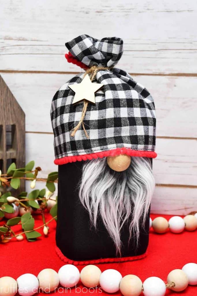 gnome treat jar with buffalo check hat and black body with a small red pompom trim made with a placemat on a holiday background