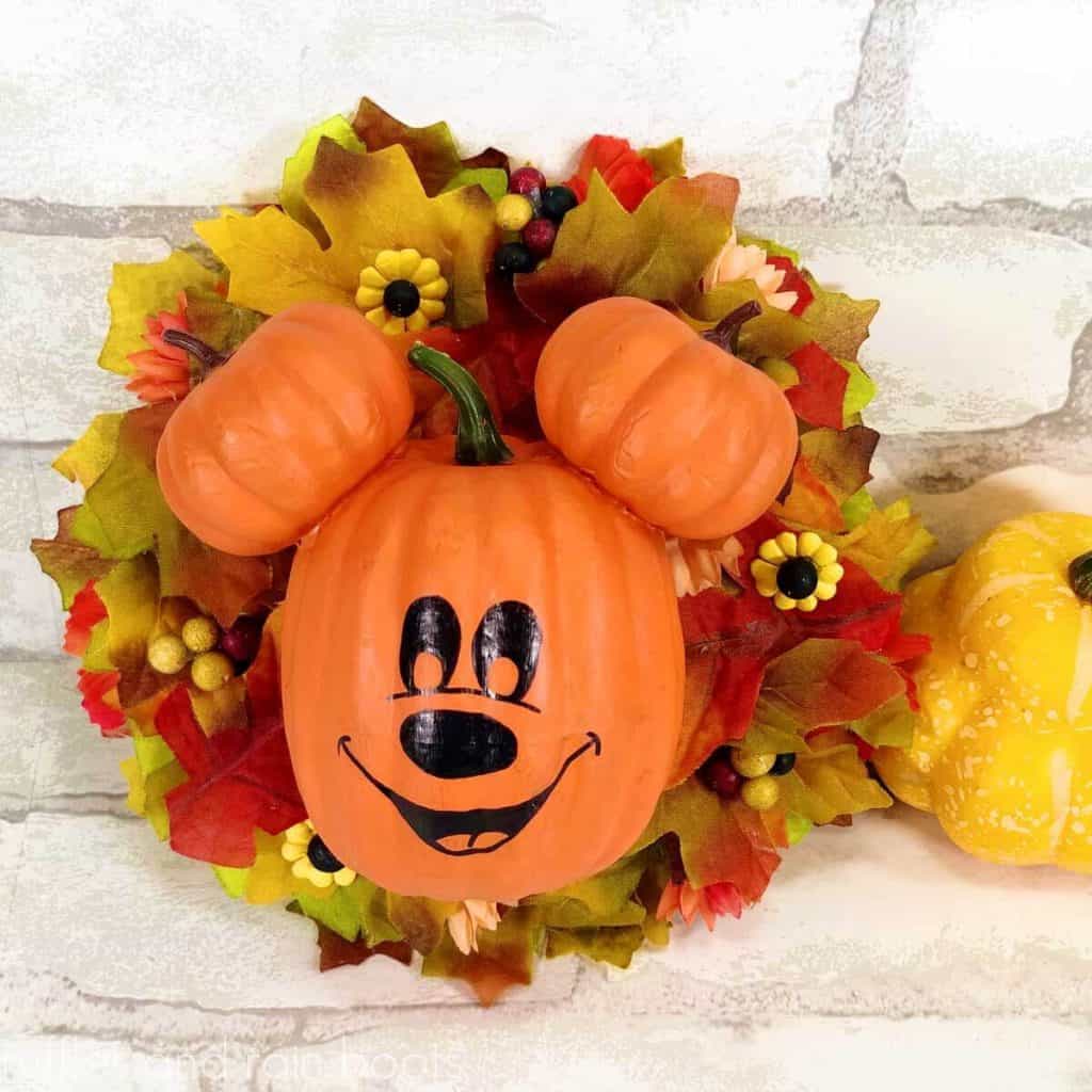 square image close up of fall Mickey Mouse pumpkin head wreath made with fake fall leaves and pumpkins
