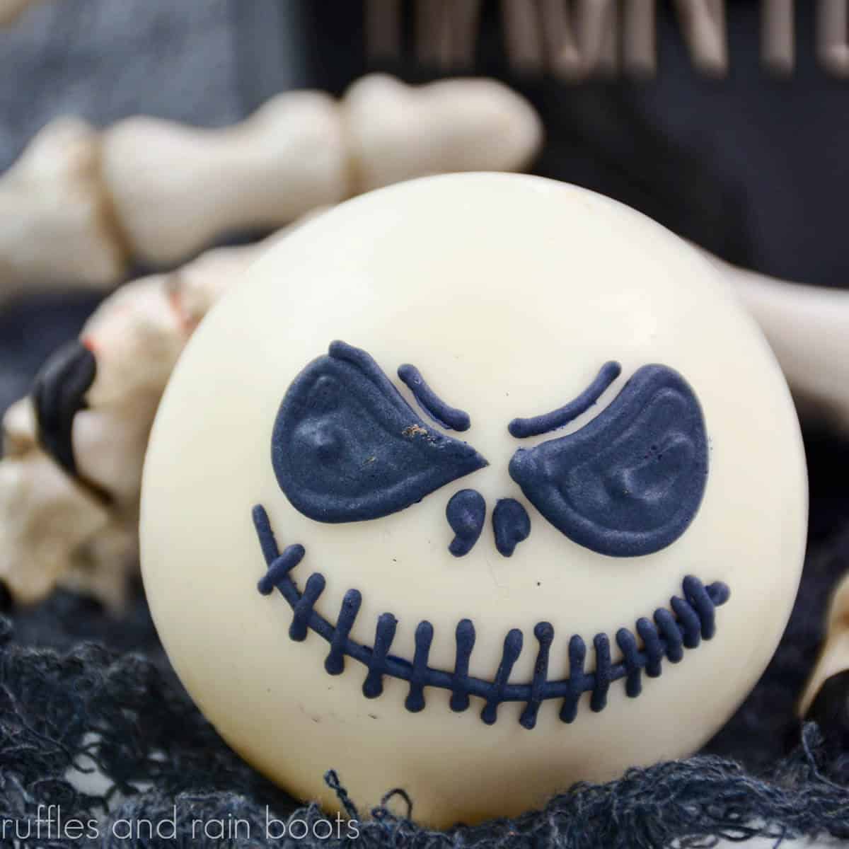 square close up image of a white hot cocoa bomb with a black royal icing face of Jack Skellington from the Nightmare Before Christmas