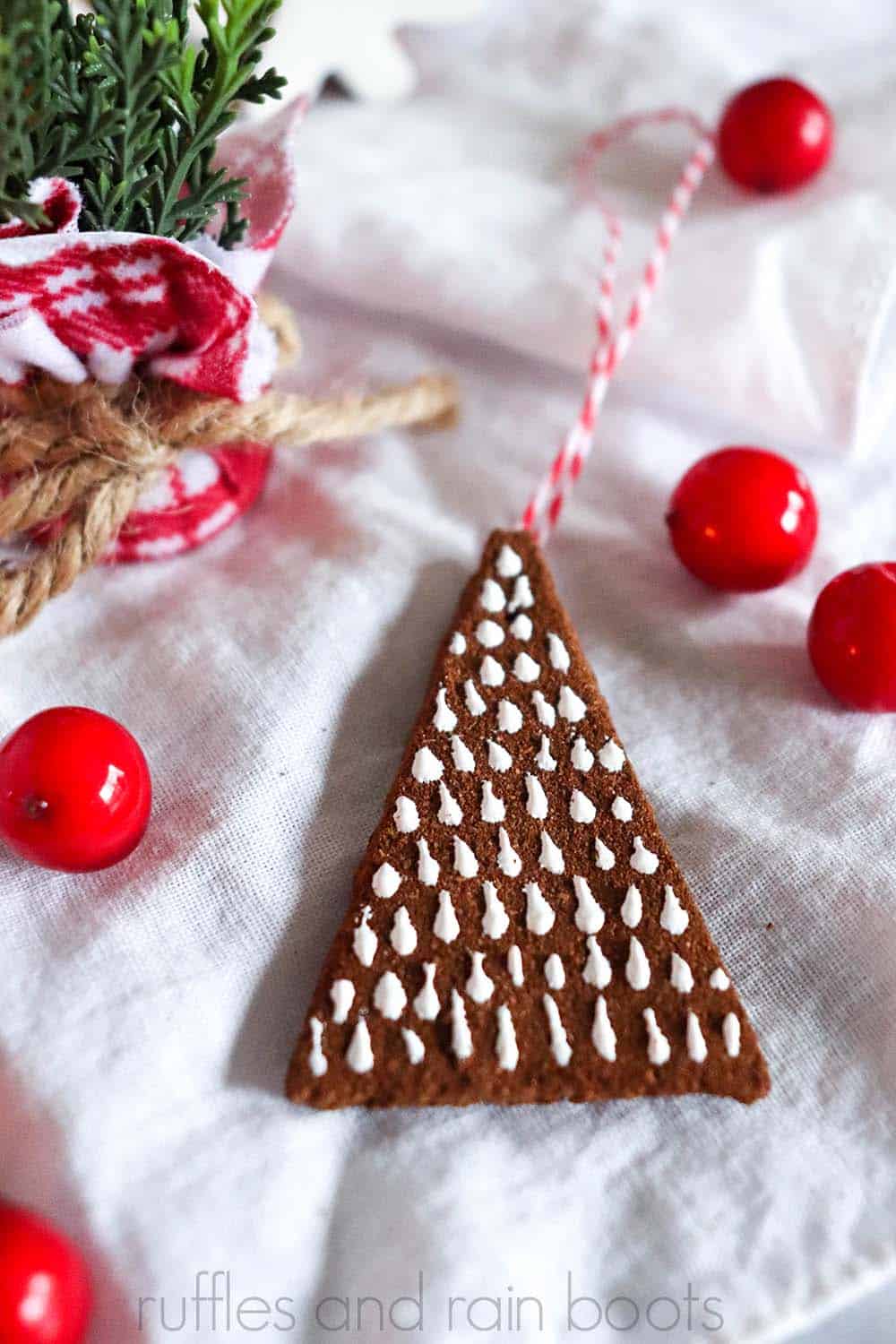 Christmas tree ornament made with no bake cinnamon spice dough recipe with red twine string on a white background with red berries and holiday pine