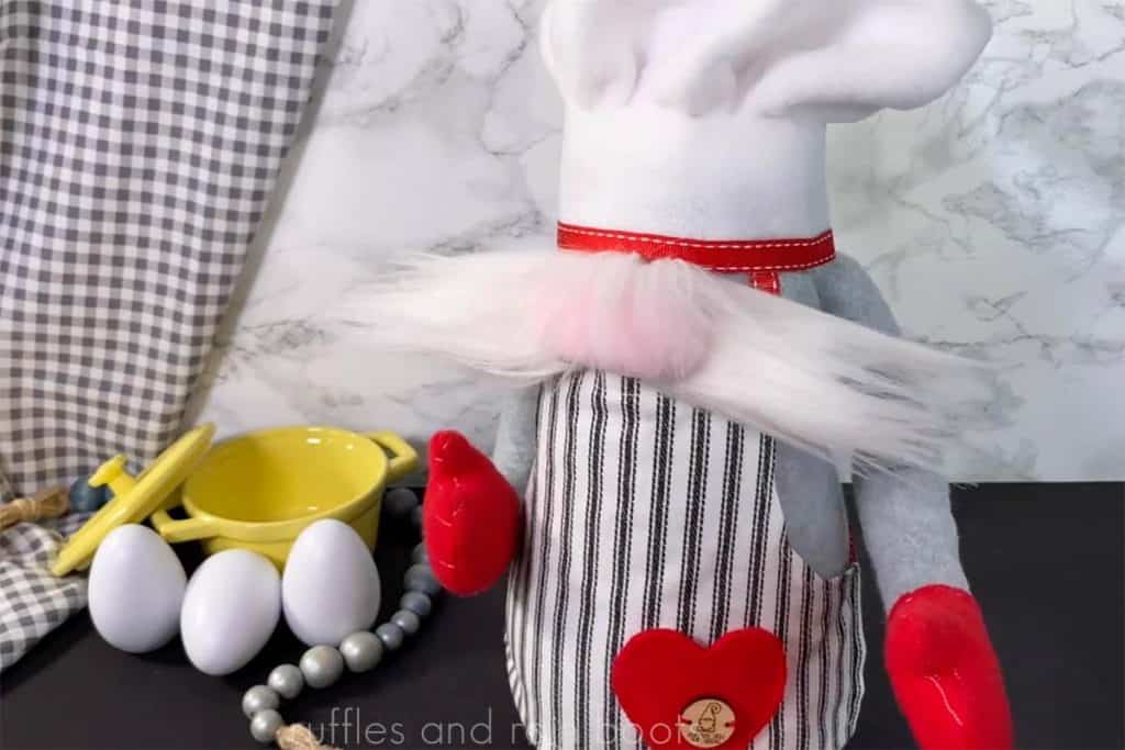 adorable chef gnome with red oven mitts and striped apron on marble background with yellow dutch oven eggs and farmhouse beads