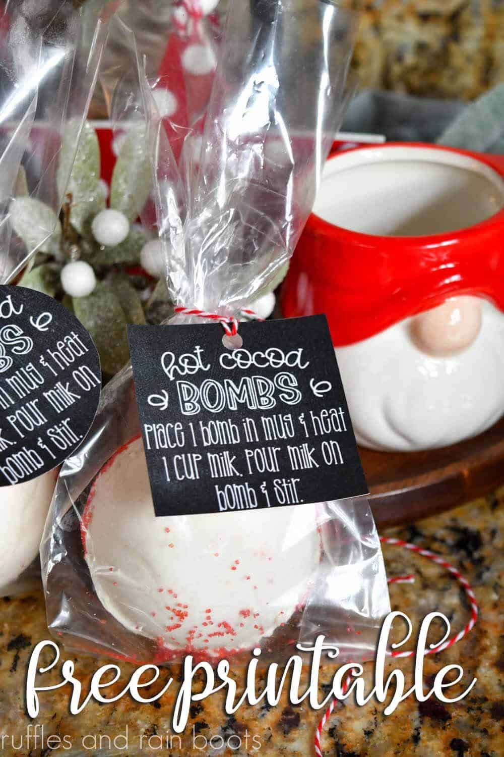 vertical image of a close up of a chalkboard style printable hot cocoa bomb gift tag label tied onto a cellophane bag with a vanilla and peppermint hot cocoa bomb in front of a gnome display