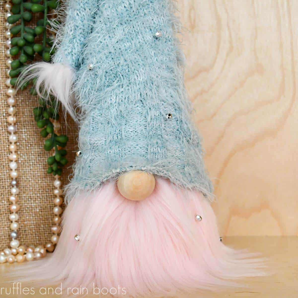 Close up image of a cone gnome made with a pink fur beard, wooden nose, and sweater sleeve hat with a diy pompom.