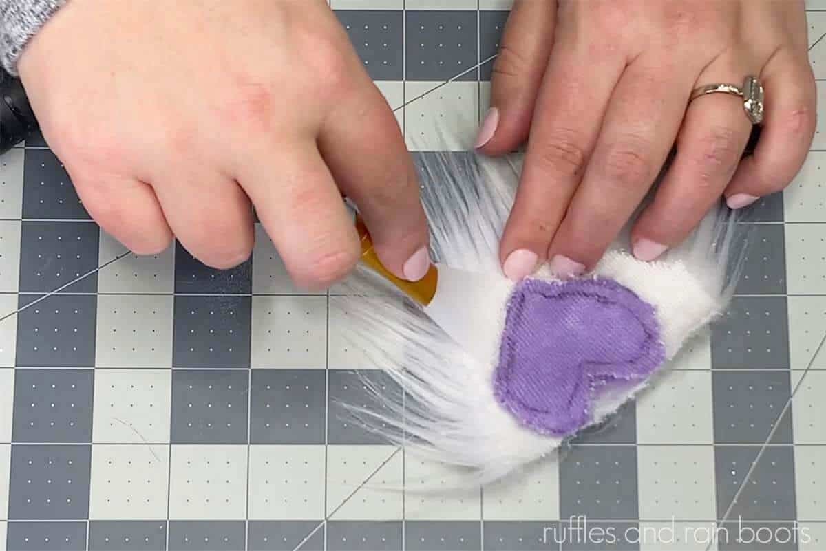 Hands holding a gnome beard made with a custom heart pattern in fur in purple and white.