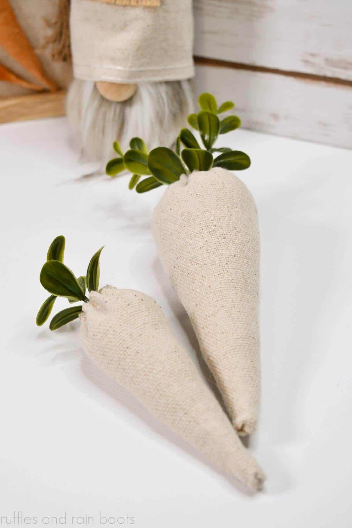 Vertical image of drop cloth carrots with boxwood greenery on a wood and white table background with small gnome and text which reads ruffles and rain boots.