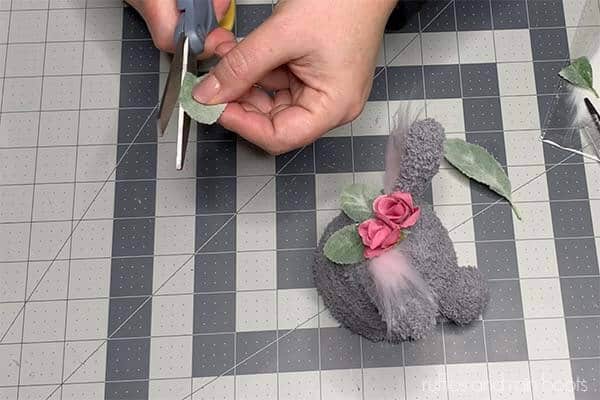 Horizontal image of a crafter cutting a lamb's ear leaf to add to floral decoration on clay pot bunny.