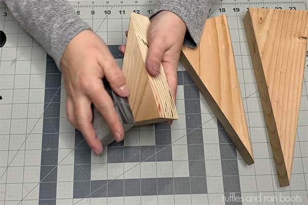 Horizontal image of a crafter using a sanding block to smooth out the wood blocks for the triangle gnomes.