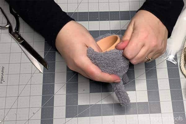 Horizontal image of a crafter pulling a gray fuzzy glove onto a 3 inch clay pot.