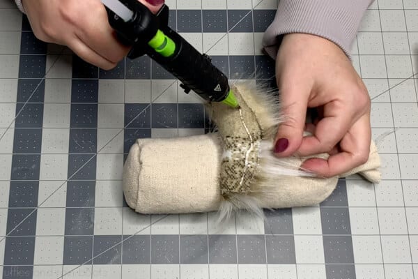 Horizontal image showing a crafter doing step 10 which is securing the gnome beard to the front of the body and fraying the top gather of drop cloth.