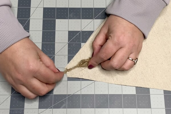 Image showing a crafter using hot glue to affix the tassel to the table at the top of the gnome hat on the right sides of the fabric.