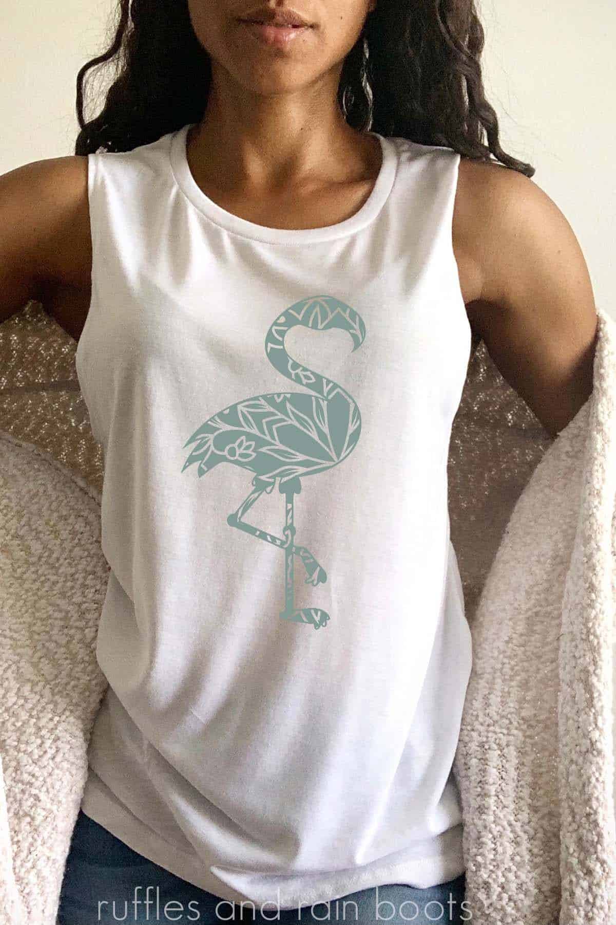 Vertical image of a beautiful woman in a beige cardigan and white muscle tank with a sage green flamingo mandala svg cut from heat transfer vinyl.