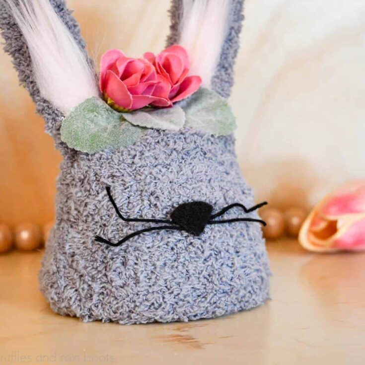 Square close up image of a gray tiered tray bunny craft made with a clay pot and a fuzzy glove with farmhouse beads and a tulip in the background.