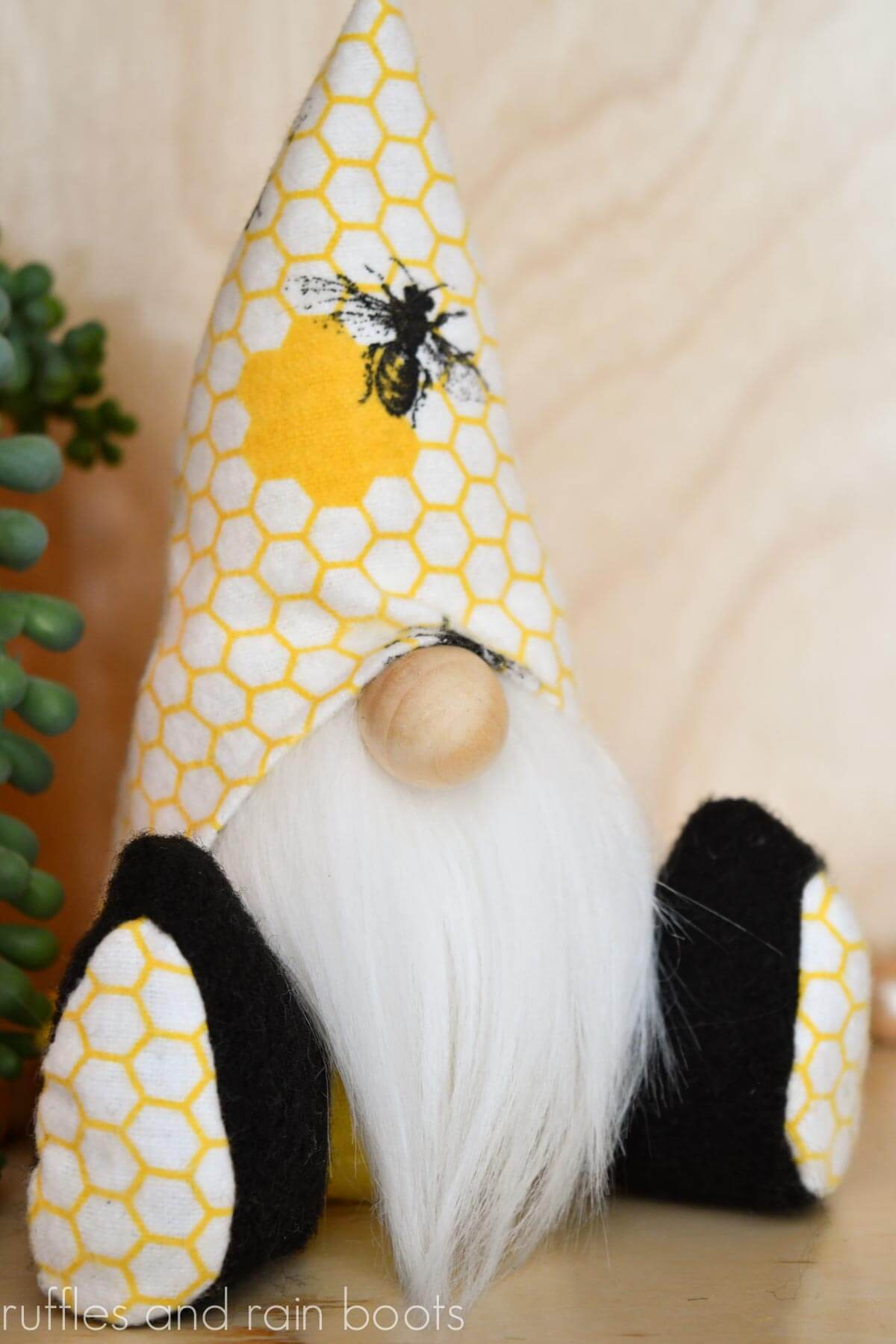 Vertical image of a tiered tray gnome made with bee flannel fabric sitting on a wood background with succulent behind.