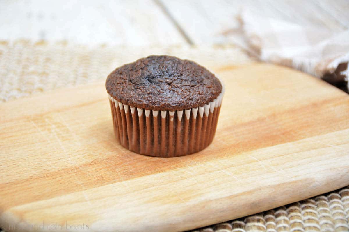 Image of a perfectly baked chocolate cupcake with mounded top on small wood cutting board.