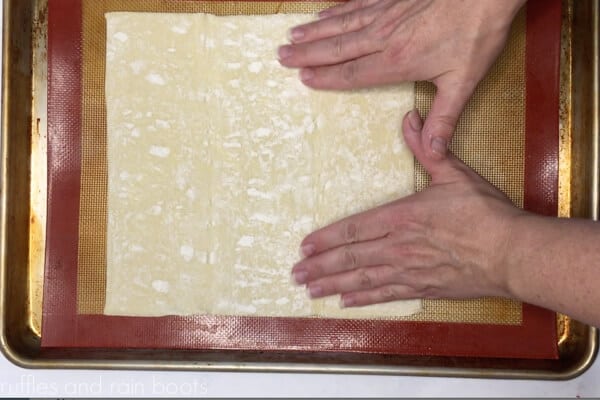 Step 1 of the PB and J pinwheels showing baker's hands unfolding a puff pastry sheet onto a Silpat placed on a baking sheet.