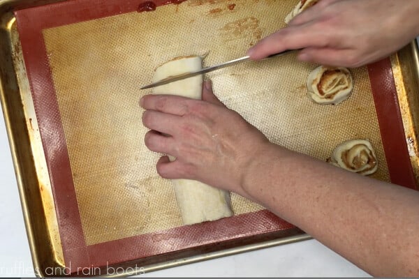 Image showing a baker cutting a puff pastry rolled log into one inch slices on the Silpat mat.
