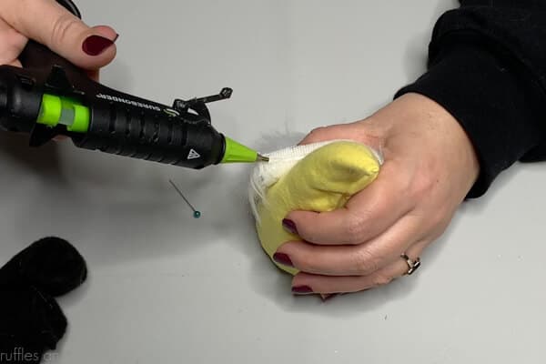 Glue gun and hot glue is being used to attach a white fur beard to a gnome body.