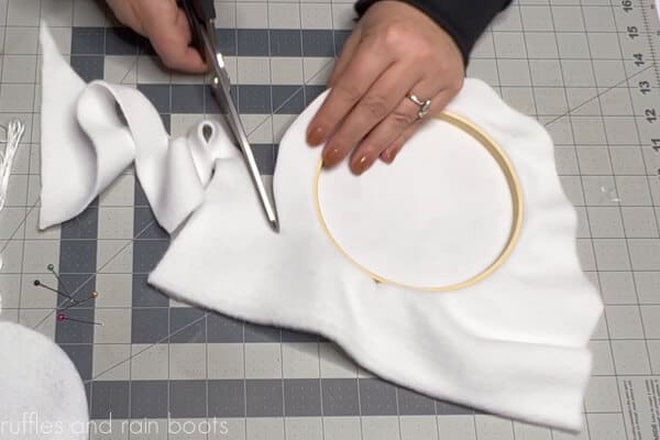 Horizontal image of crafter cutting a border around the embroidery hoop and sublimated fleece fabric.
