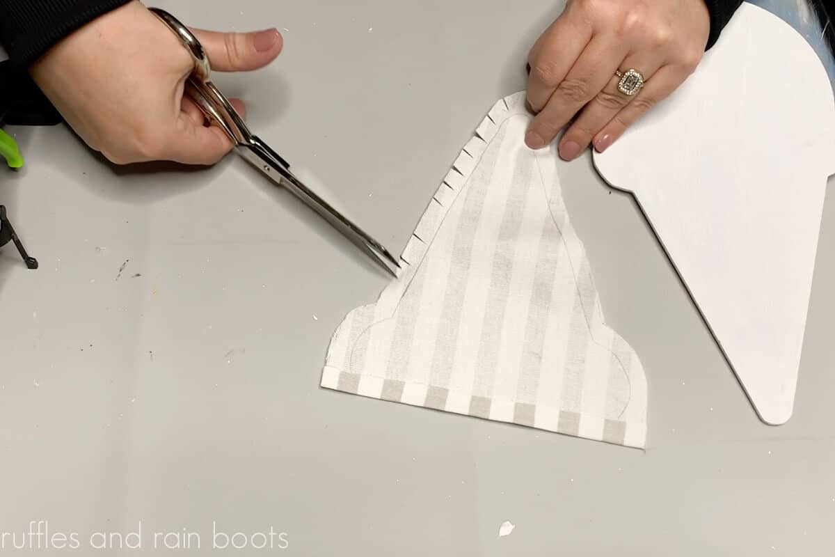 Crafter using silver scissors to cut slits into a gnome hat to adhere to the all hanging.