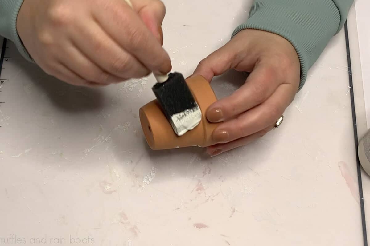 Crafter using a foam brush and chalk paint to coat a mini clay pot planter from the Dollar Tree.
