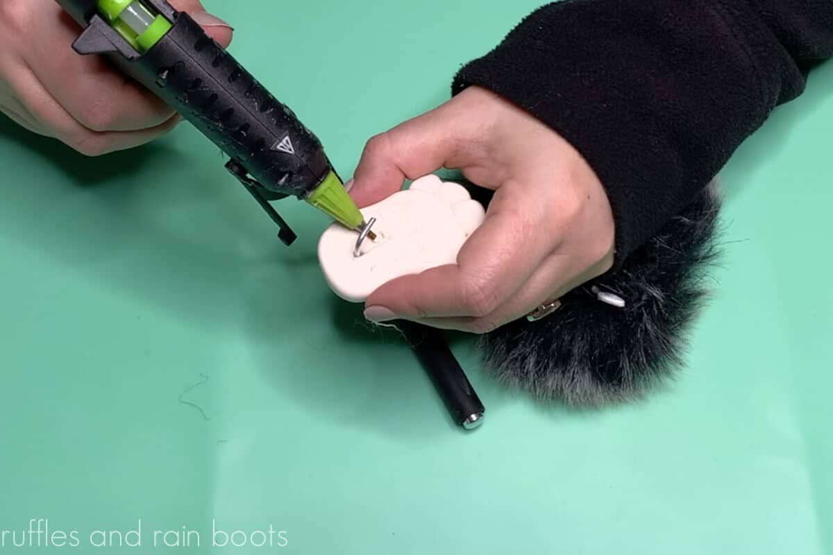 Crafter gluing the wire legs into the white clay feet with a detail tip hot glue gun on a teal silicone mat.