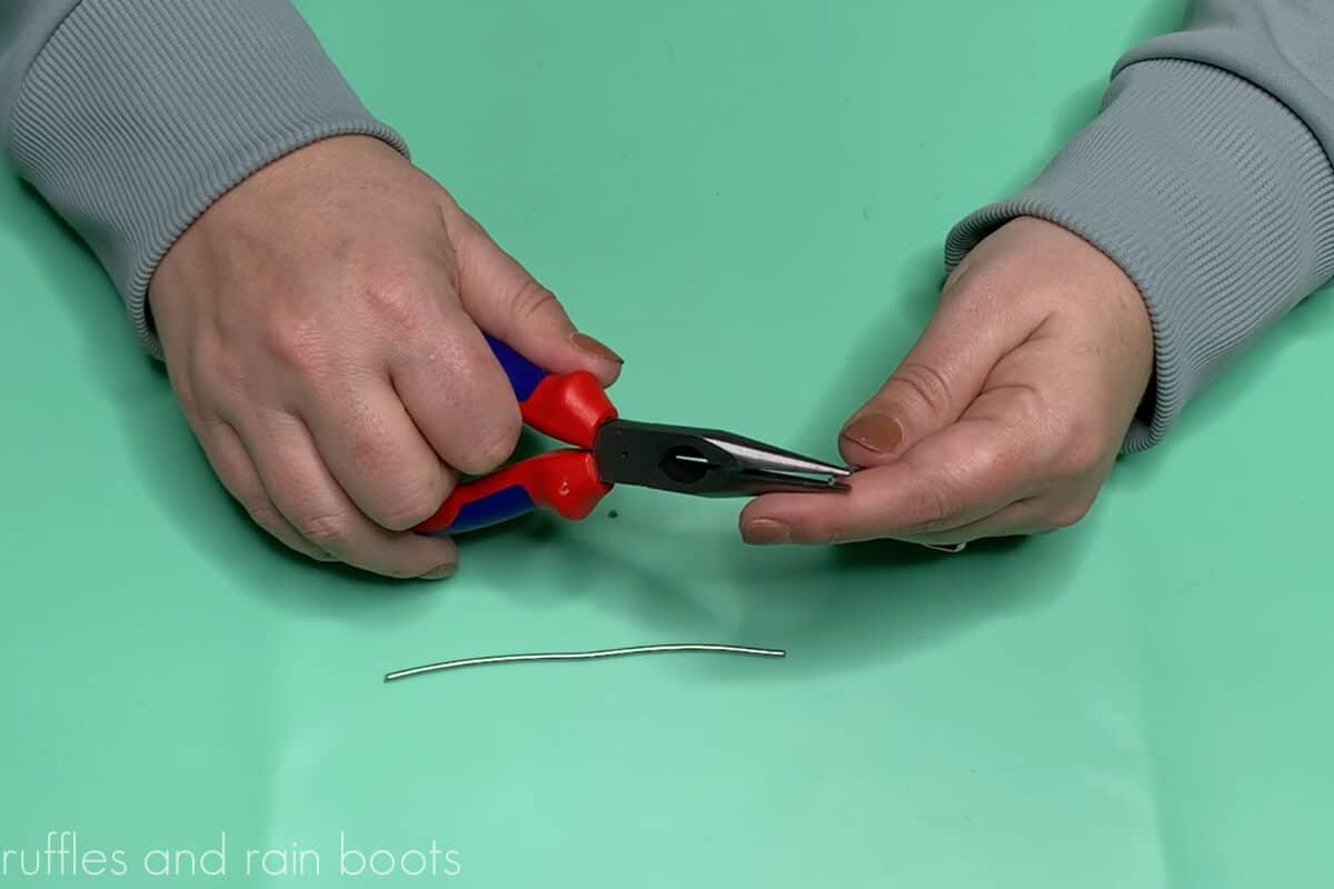 Crafter hands on teal background showing how to use pliers to bend wire to secure legs in mini gnome DIY.
