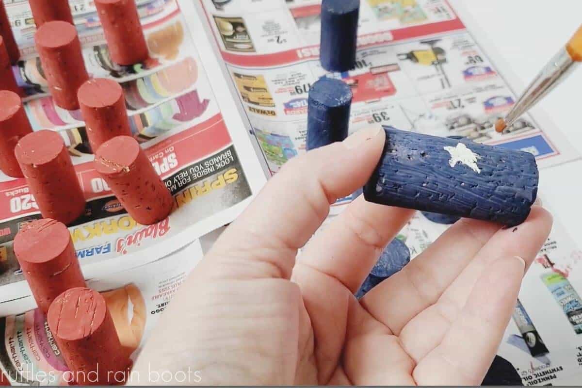 Crafter using white acrylic paint to add a star to the blue corks.