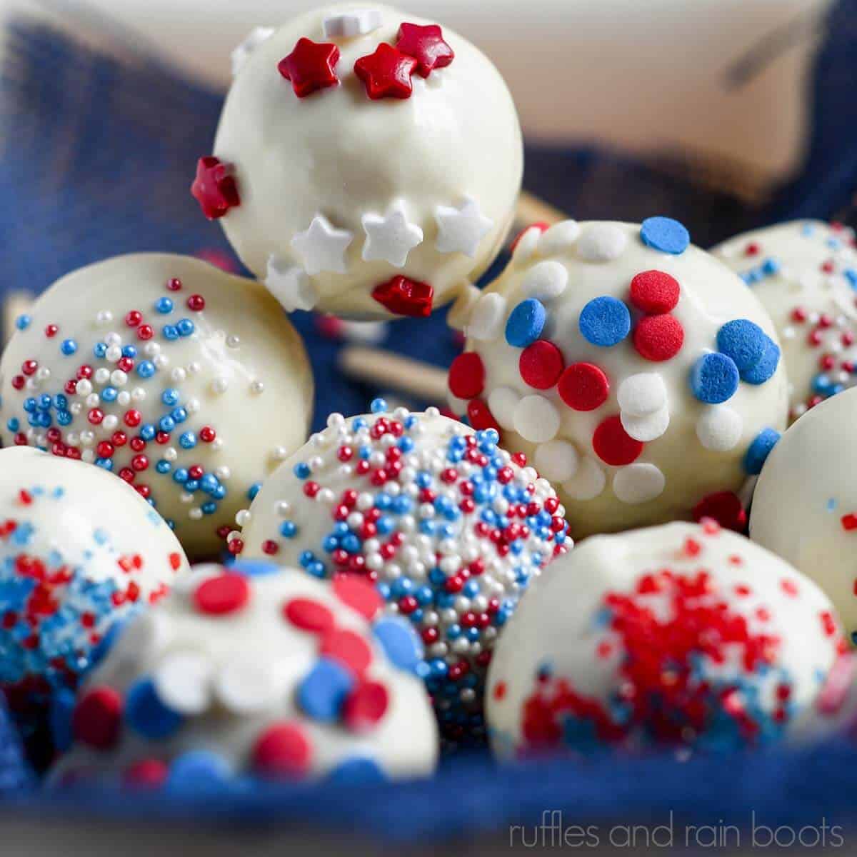 Square close up image of red, white, and blue July 4th cake pops stacked in a basket lined with a blue kitchen towel.
