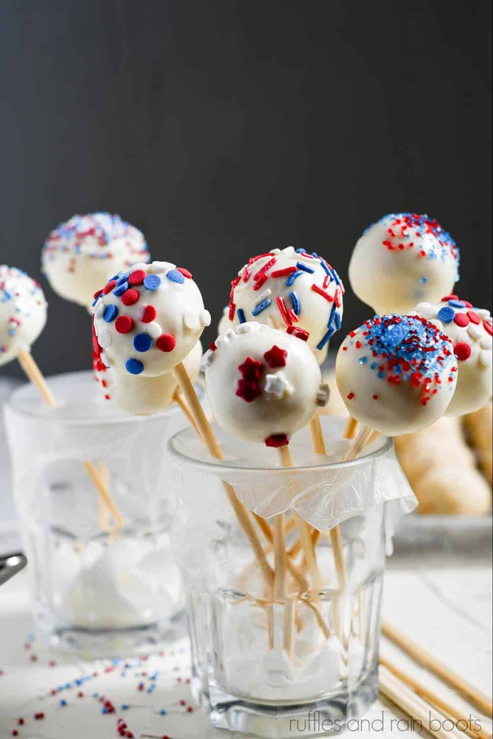 Vertical image of red, white, and blue July 4th cake pops dessert standing up in small glasses.
