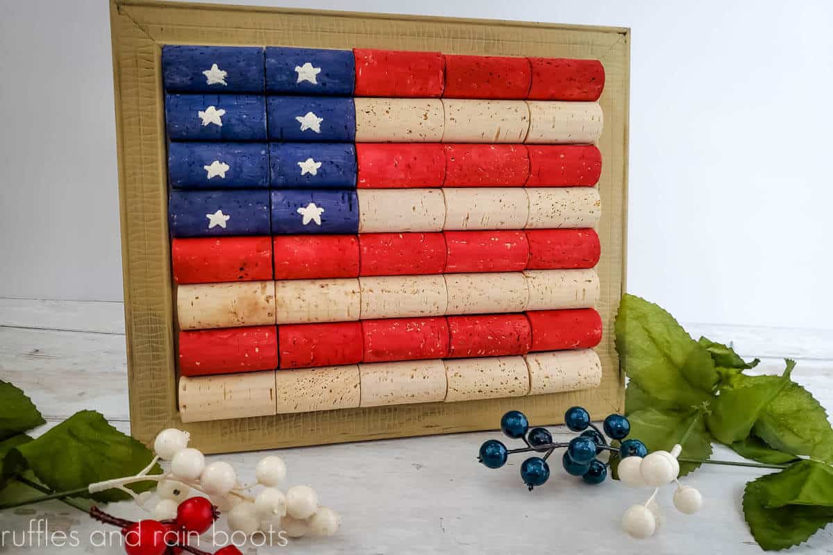Horizontal image of wine cork flag in muted red, natural, and blue painted corks in a frame on a white background.