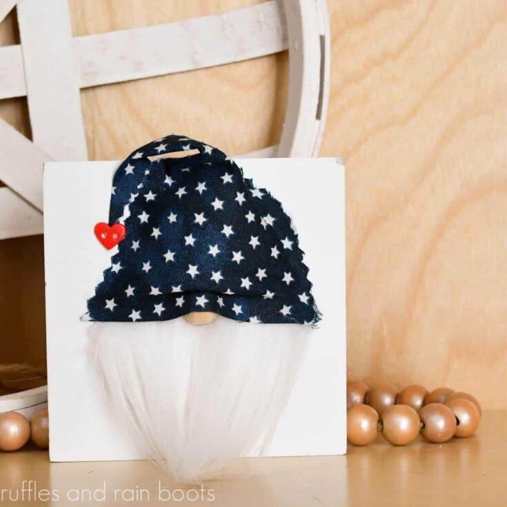 Square image of a blue star gnome sign made for Independence Day sitting against a white tobacco basket and farmhouse beads with a light wood background.