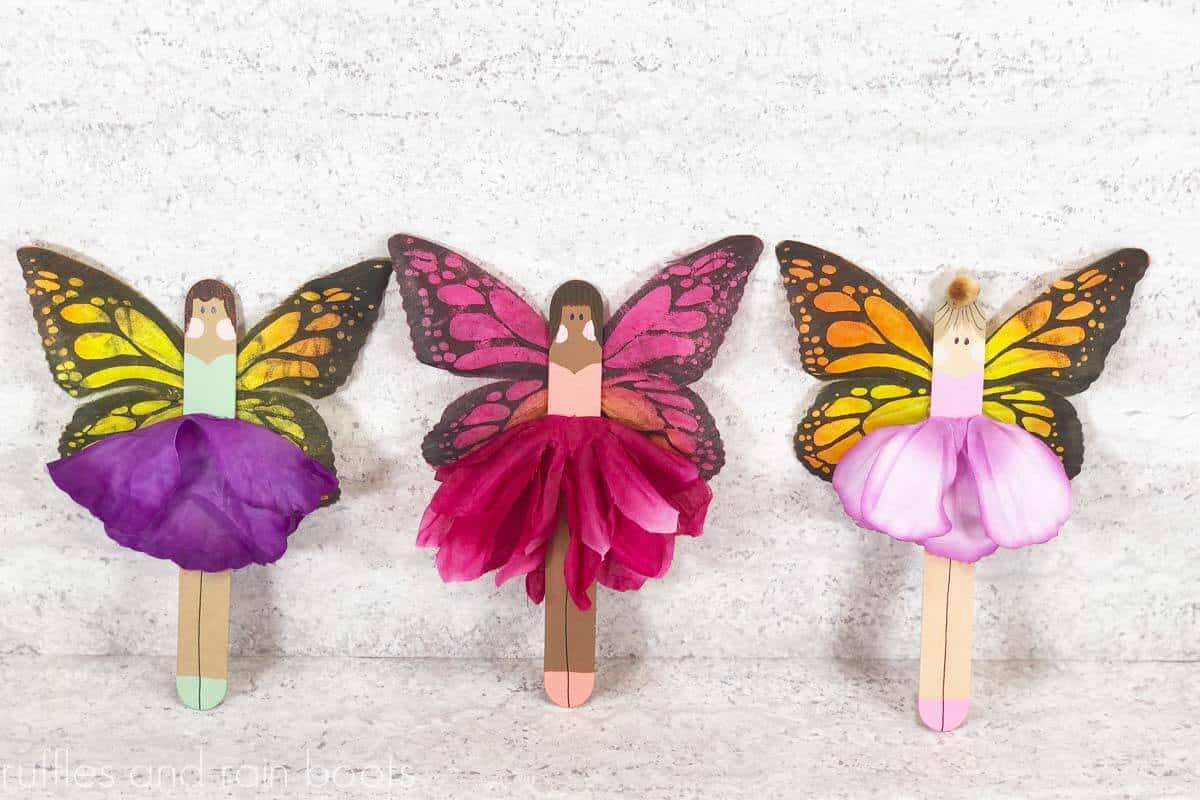 Horizontal image showing a craft stick fairy trio made with popsicle sticks, flowers, and butterfly wings from the dollar tree.