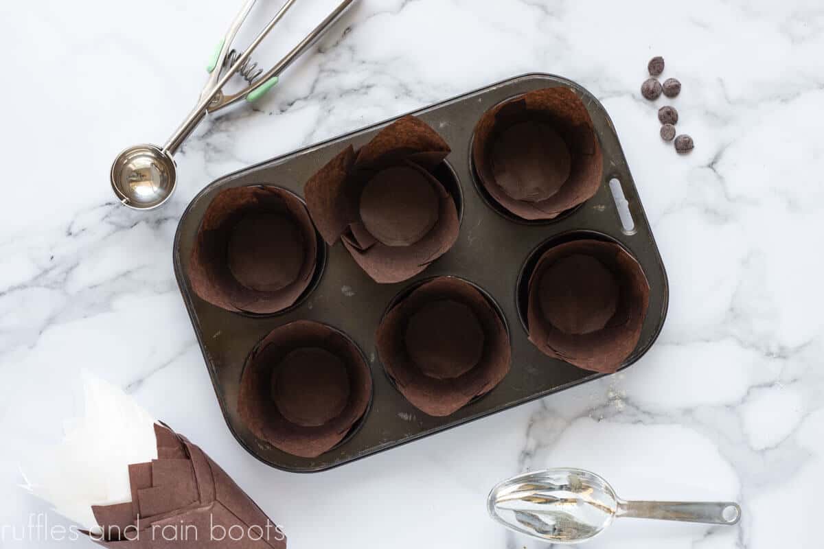 Brown muffin liners in a metal cupcake pan on a marble island counter top.