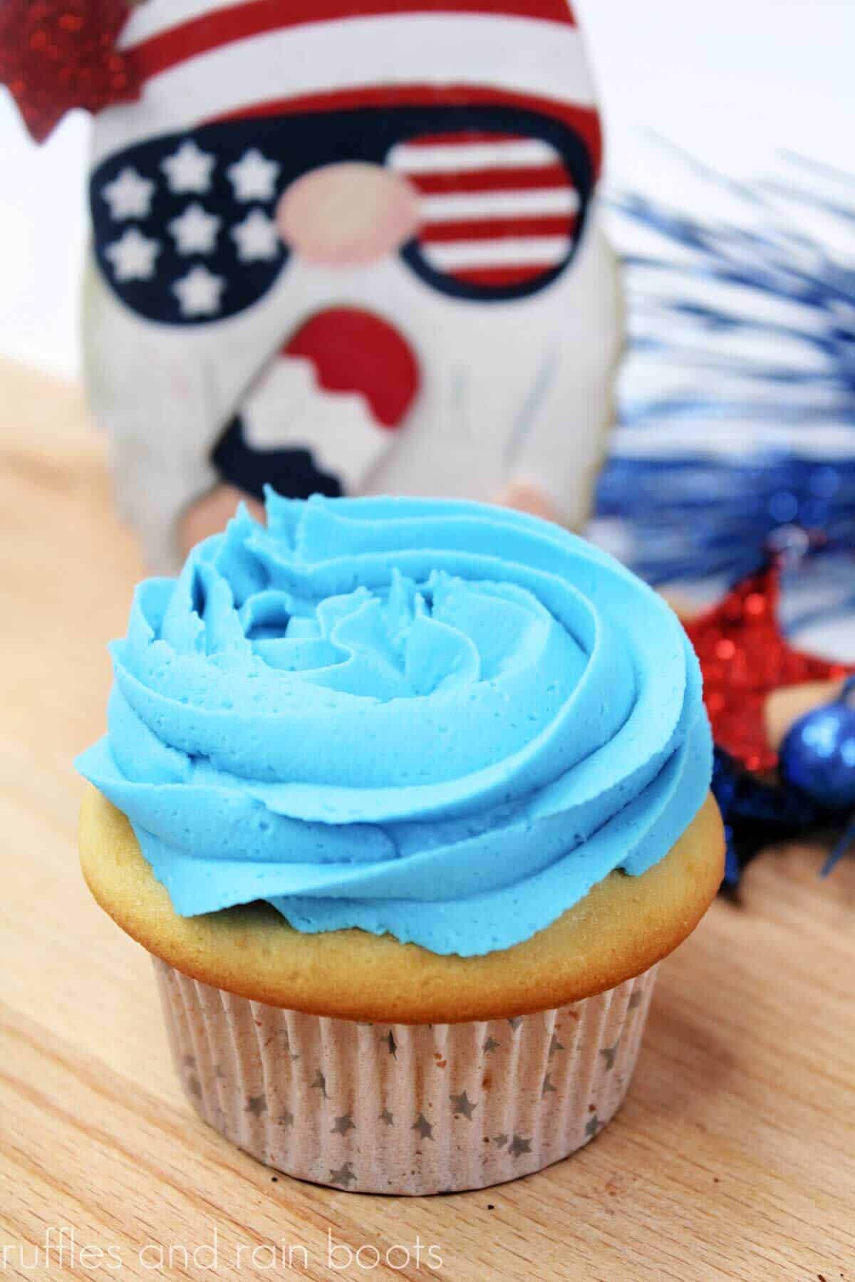 Vanilla cupcake with one layer of blue buttercream frosting with a patriotic gnome in the background.