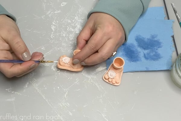 Crafter painting with white paint to prime 3D printed gnome feet with flip flops.
