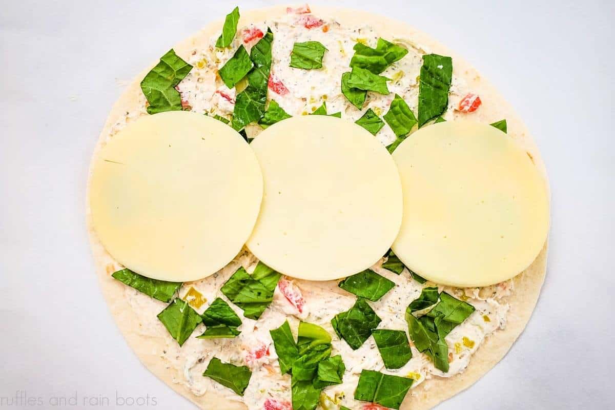 Image showing the sliced cheese on the center of the tortilla of the Italian pinwheel sandwich recipe.