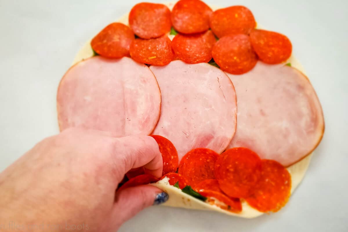 Home chef showing to spread salami and pepperoni onto tortilla.