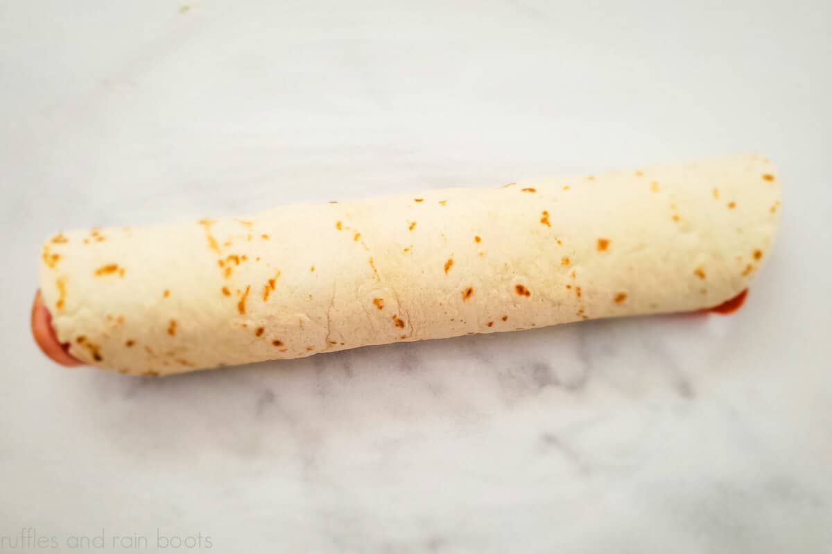 A log of a tortilla rolled with Italian meats on a marble counter.