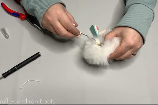 Crafter using glue to secure the loop of the leg wire to the inside back fabric of the fur pompom.