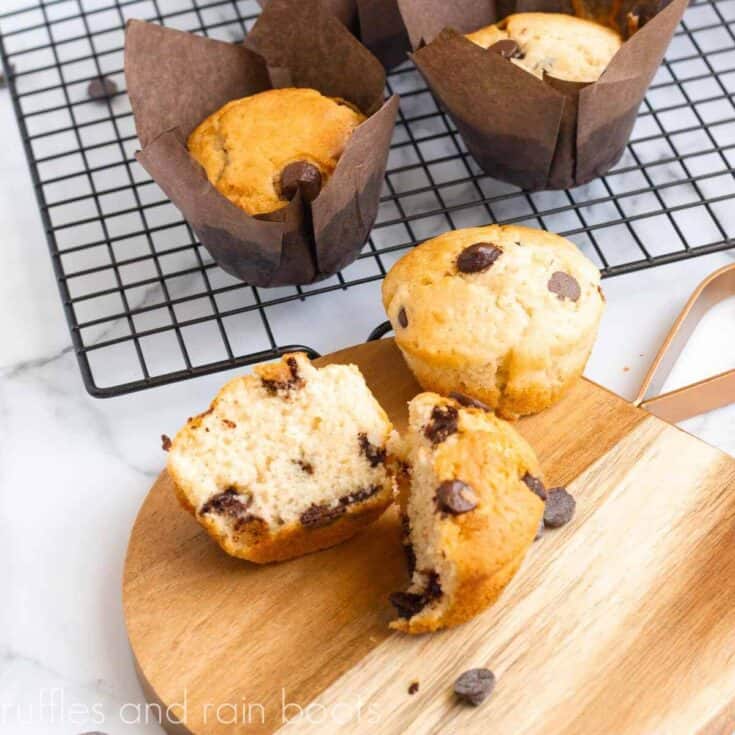 Split chocolate chip muffin on wood cutting board on marble counter top cooling.